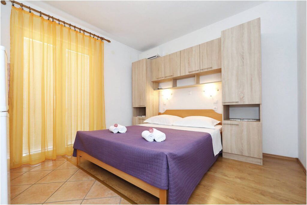 Studio apartment interior at Villa Rajna showing a queen-size bed, kitchenette, and private balcony access.